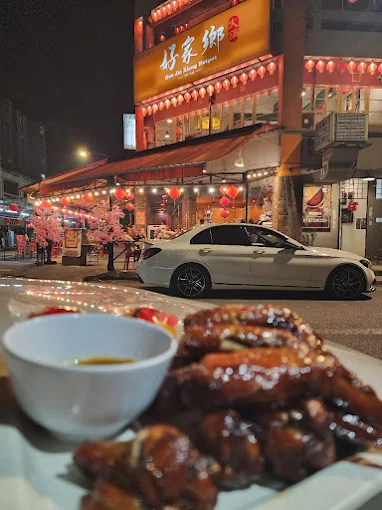 甲洞 Bandar Menjalara 夜间的 Hometown Hotpot 店面,前景为两姐妹烧鸡翼